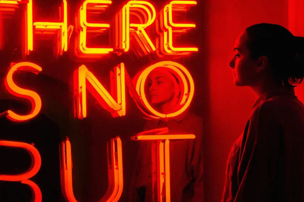 Kvinne betrakter et kunstverk i neon, med teksten «There is no but»