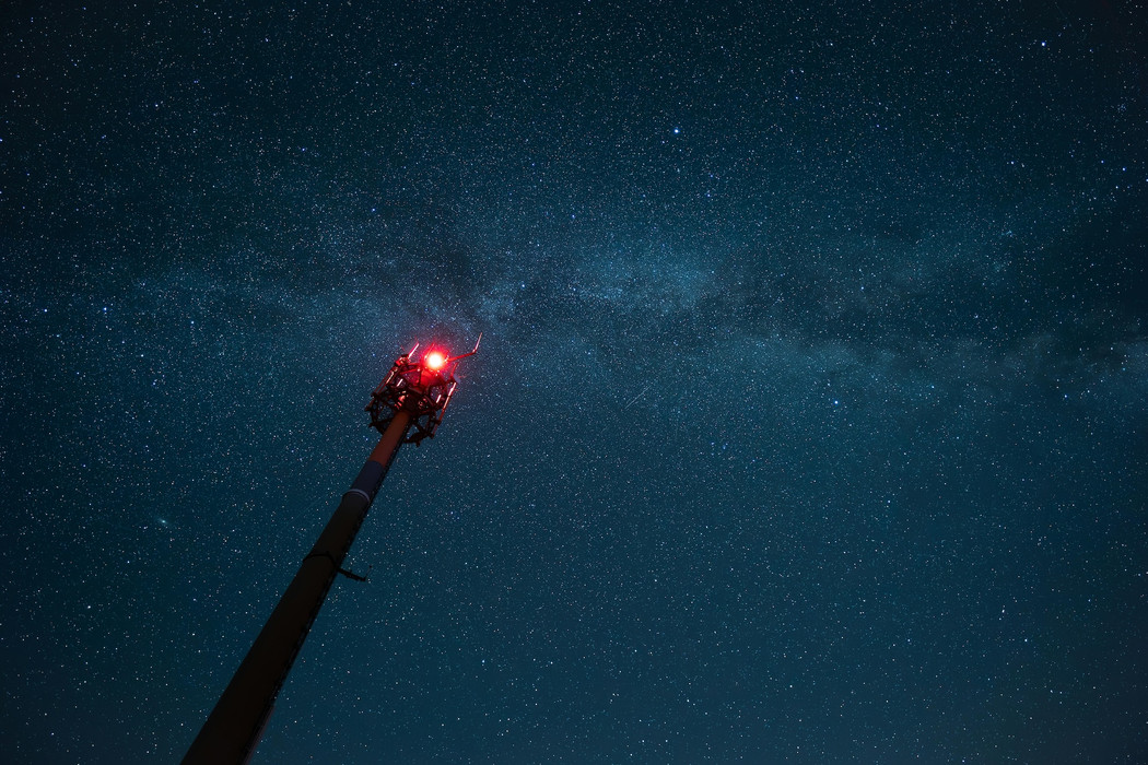 A broadcast tower looming diagonally into the image, from bottom left towards the centre of the image, towards a starry night sky. 