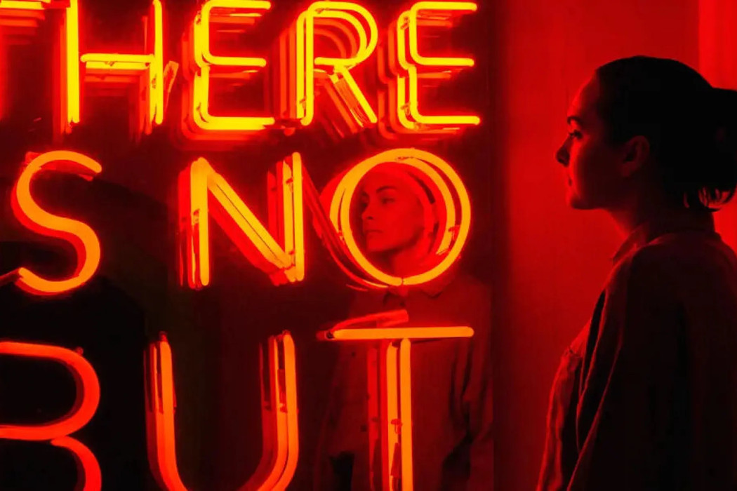 Kvinne betrakter et kunstverk i neon, med teksten «There is no but»