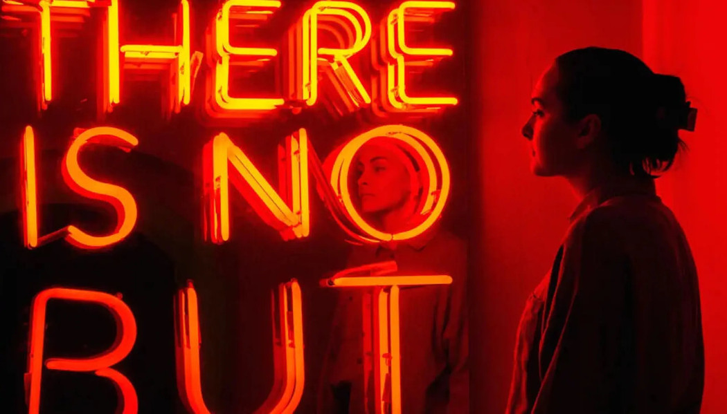 Kvinne betrakter et kunstverk i neon, med teksten «There is no but»