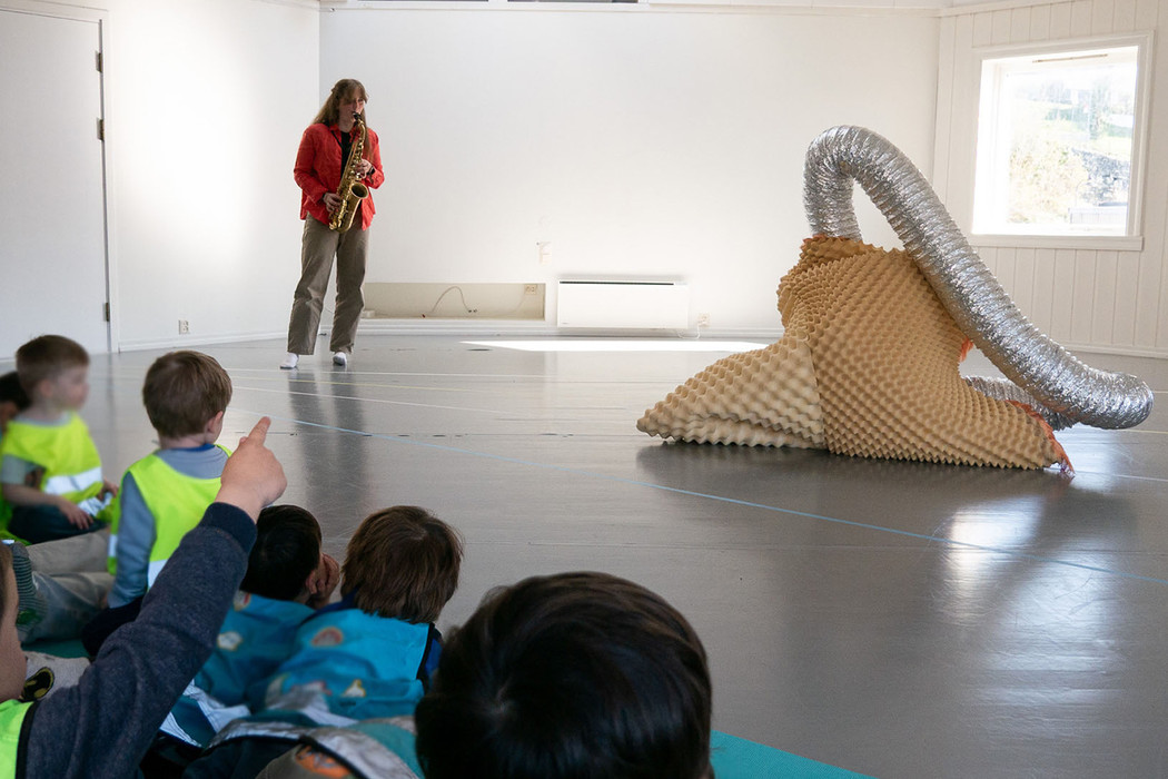 A musicican plays the saxofon while an amorph object, a fantastical creature, moves to the music. Children are the musical performance. 